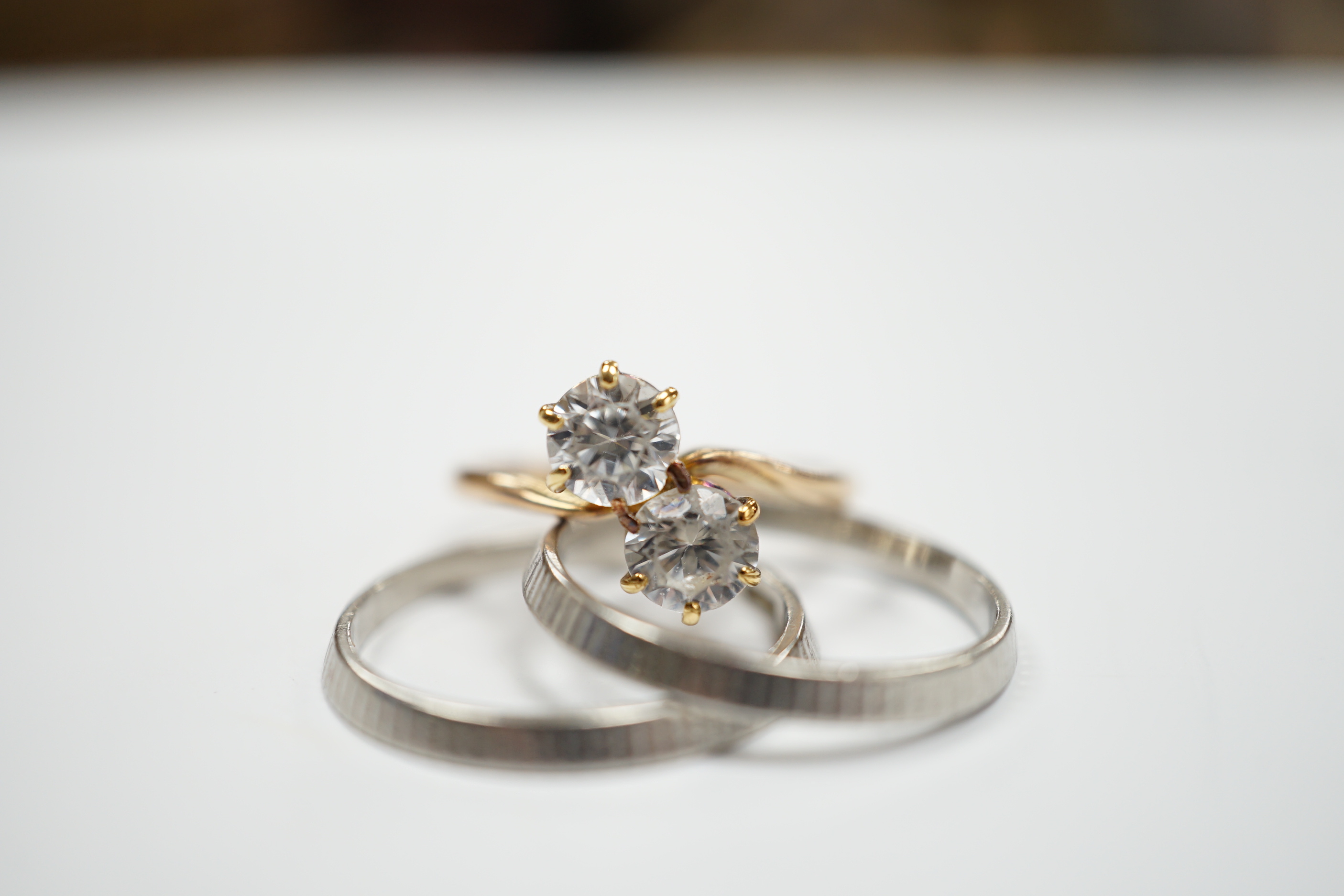 Two white metal bands (stamped platinum) with milled finish, 5.4 grams, together with a 14k and two stone white zircon set crossover ring, gross weight 2.3 grams.